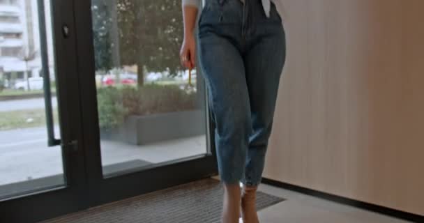 A young businesswoman in casual business attire walks briskly through a sleek office hallway, holding documents and a pencil, exuding a sense of purpose and determination in her stride. - Footage, Video