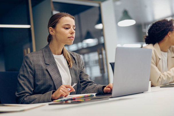 Mooie vrouwelijke freelancer werkt aan laptop terwijl hij in moderne coworking zit. Begrip "werken op afstand" - Foto, afbeelding