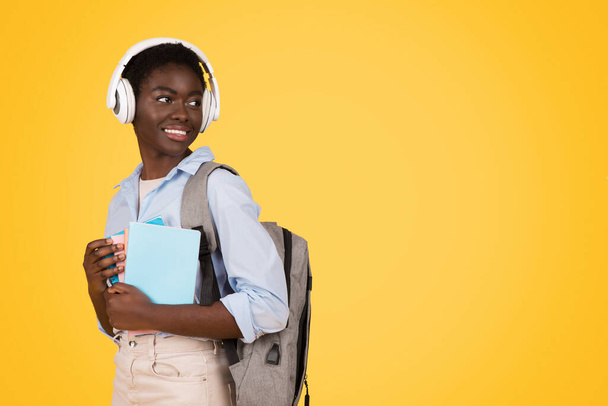 No fundo do pensamento, esta estudante afro-americana representa a atitude reflexiva da Geração Z enquanto segura seus cadernos Isolada contra um fundo amarelo, espaço de cópia - Foto, Imagem