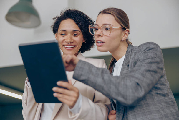 Wesołe kobiety biznesu ludzi stojących w nowoczesnym coworking i korzystania z tabletu cyfrowego razem - Zdjęcie, obraz
