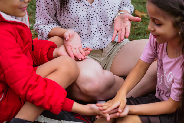 Mezinárodní den dětí. Latinská matka se baví se svými malými dětmi venku. Seděli na zemi a hráli si s rukama. Pojem rodina. Svobodná matka se dvěma malými dětmi. - Fotografie, Obrázek