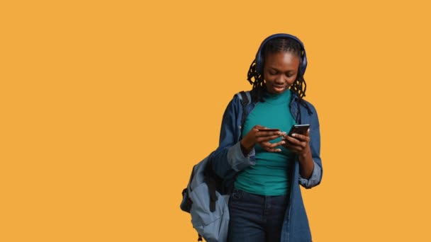 African american teenager adding payment method on website, isolated over studio background. Young girl wearing headphones, doing internet shopping, typing credit card information on phone, camera B - Footage, Video
