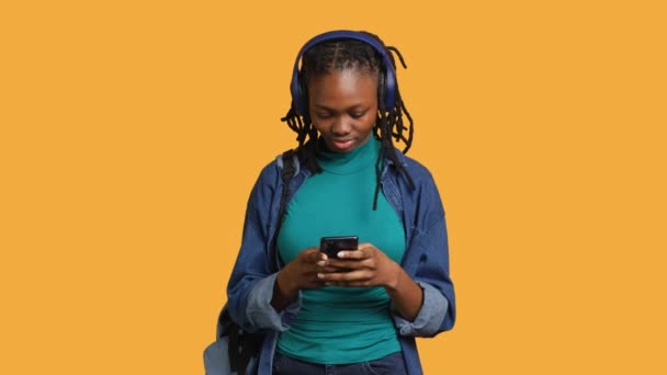 Smiling woman discussing with friends during teleconference meeting using smartphone and headphones, studio background. Girl catching up with mates during online videocall on mobile phone - Footage, Video