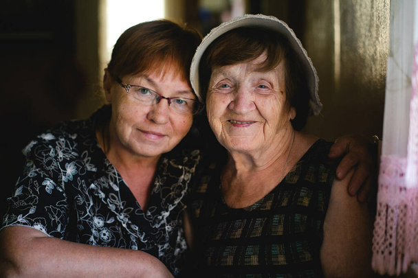 Een oudere vrouw en haar volwassen dochter delen een teder moment in het portret, een weerspiegeling van het verstrijken van de tijd en de blijvende band tussen generaties.. - Foto, afbeelding