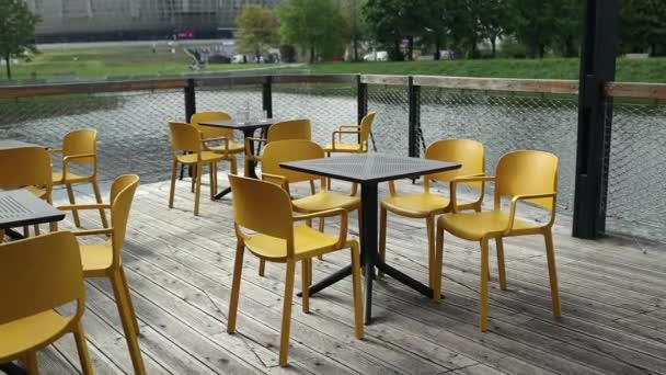Black tables with yellow modern charis in cafe on the street. Empty cafe in the summer morning. Modern outdoor cafe. Street cafe. Modern Terrace. Empty restaurant. High quality FullHD footage - Footage, Video