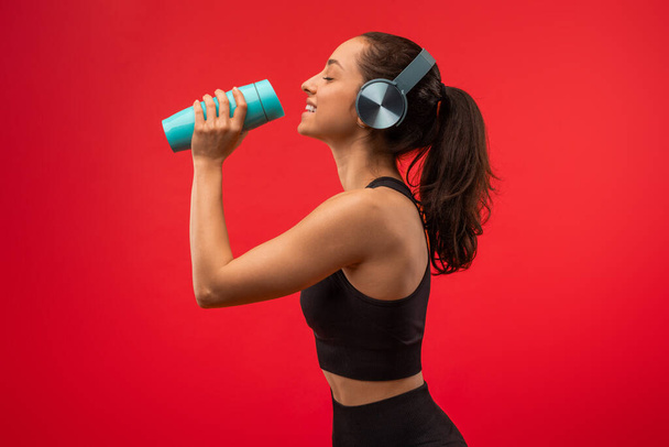 A woman wearing headphones is holding a blue cup to her lips, taking a sip of a beverage. She appears focused on enjoying her drink. - Photo, Image