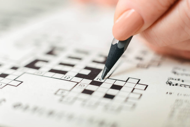 人が積極的にクロスワードパズルに従事し,鉛筆を持ち,慎重に文字で箱に詰め込まれているのが見られます. クロスワードグリッドが表示され,空白と満たされた正方形のミックスが表示されます.. - 写真・画像