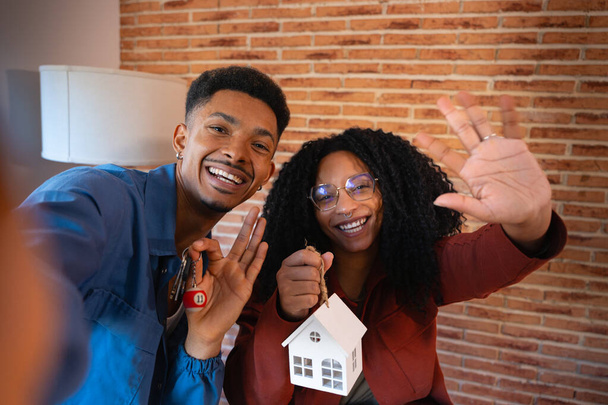 Homme et femme avec mini maison et clés de leur nouvelle maison faisant un appel vidéo à leurs amis pour annoncer qu'ils ont une nouvelle maison. - Photo, image