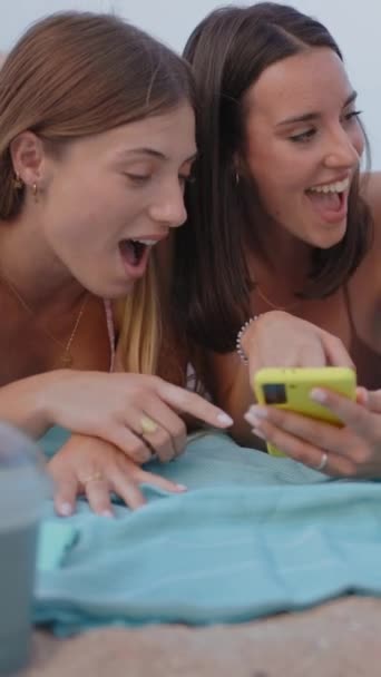 Κάθετα. Ομάδα από τρεις χαμογελαστές νεαρές γυναίκες που χρησιμοποιούν την εφαρμογή κινητού τηλεφώνου που βρίσκεται στην παραλία. Χαρούμενα κορίτσια που απολαμβάνουν ελεύθερο χρόνο το Σαββατοκύριακο. Έννοια των καλοκαιρινών διακοπών, τους φίλους και την κοινωνική δικτύωση στη γενιά z - Πλάνα, βίντεο