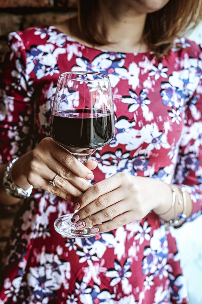 Una mujer elegantemente sostiene una copa de vino tinto en una elegante cena. - Foto, imagen