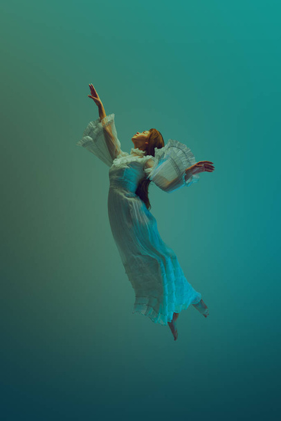 Mujer joven en vestido vintage blanco emana sensación de profunda paz y tranquilidad, llegando al cielo desde debajo del agua. Concepto de serenidad y calma, libertad y levitación, sueño, surrealidad, fantasía. Anuncio - Foto, imagen