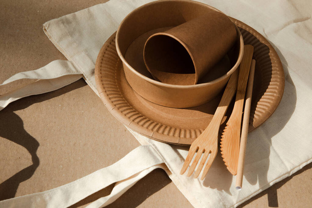 Una serie di utensili di carta e posate in legno in sacchetto di tessuto su uno sfondo marrone. Eco-friendly, zero rifiuti concetto. Vista dall'alto - Foto, immagini