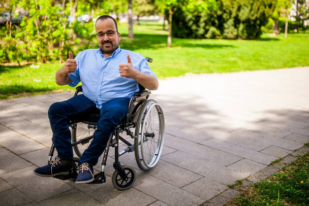 Portrait d'homme heureux en fauteuil roulant. Il profite d'une journée ensoleillée au parc de la ville. - Photo, image