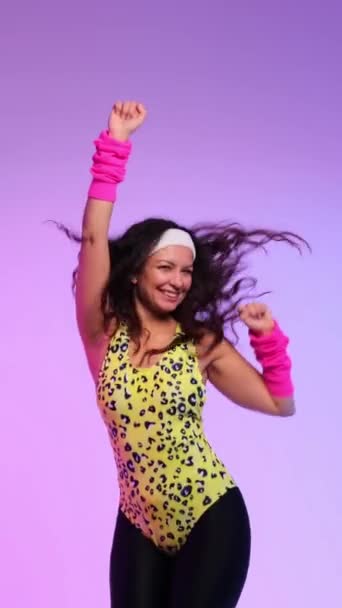 Розваги і позитивна кавказька жінка в ретро спортивному одязі грайливо танцює на фіолетовому тлі до старовинної музики 90-х років. Вертикальне відео. - Кадри, відео