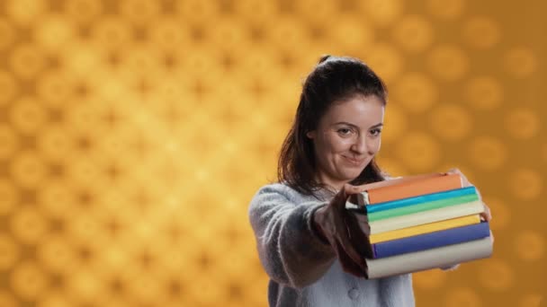 Portrait of friendly woman offering stack of textbooks useful for school exam, isolated over studio background. Merry person giving pile of books, recommending them for university assessment, camera A - Footage, Video