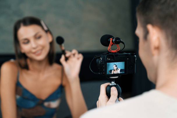 Mann filmt Video über junge Frau, die Schönheits- und Kosmetikvideos für soziale Medien macht. Beauty-Bloggerin lächelt in die Kamera, während sie dem Publikum oder ihren Followern zeigt, wie man Schönheitspflege betreibt. Enthüllung - Foto, Bild