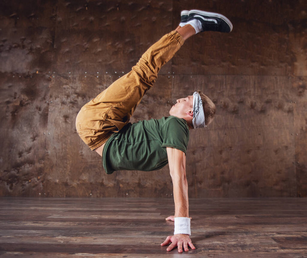 Молодой человек танцует брейк-данс на фоне стены, выполняя трюки
 - Фото, изображение
