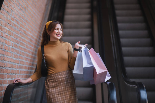 Eine Frau steht mit Einkaufstüten in der Hand auf einer Rolltreppe. - Foto, Bild