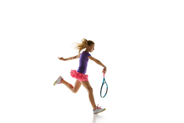 Competitive young girl, female athlete training passing shot in motion against white studio background. Model in comfortable uniform. Concept of professional sport, movement, tournament, action. Ad - Photo, Image