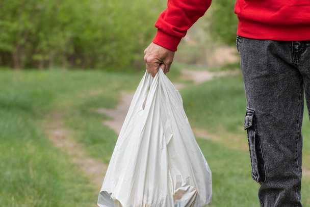 Muž drží bílý plastový sáček v ruce.Environmentální problém znečištění plastových odpadků. - Fotografie, Obrázek