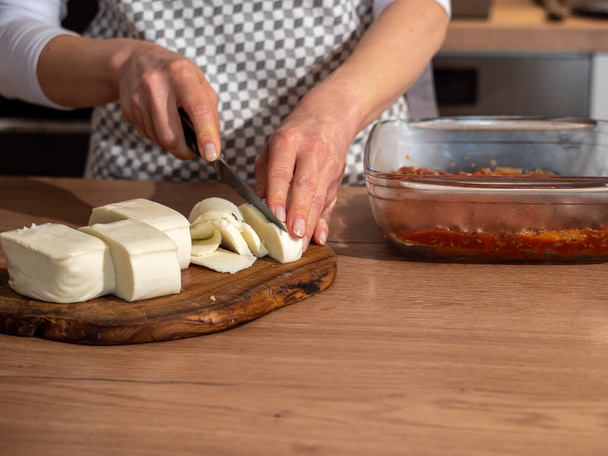 corte de queijo mussarela italiano em uma tábua de madeira, mãos femininas com uma faca, foto cores quentes - Foto, Imagem