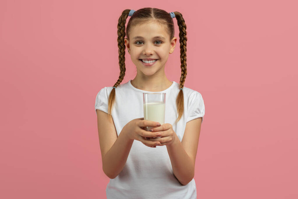 Дівчина тримає склянку молока, приємно посміхаючись, ізольована на рожевому фоні, зображуючи концепцію здорового способу життя - Фото, зображення