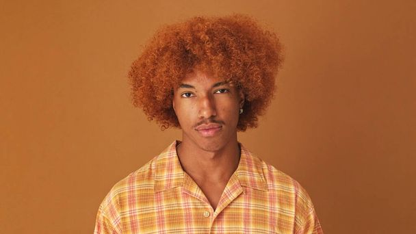Close up, stylish curly guy looking at the camera listens and strongly disagrees, isolated on brown background in the studio - 写真・画像