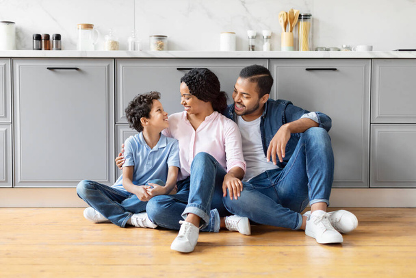 Amar a la familia negra compartiendo un momento de conexión mientras está sentada en el piso de la cocina, evocando calidez y afecto - Foto, imagen