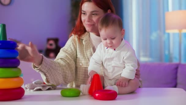 modern young female parent with a small child has fun playing with colorful educational toys making video for her blog on smartphone video camera - Footage, Video
