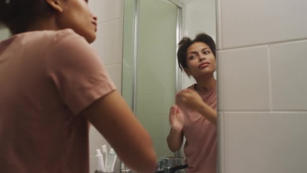 Zoom schot van jong slaperig meisje kijken naar haar reflectie in de badkamer spiegel en wrijven gezwollen gezicht na het wakker worden in de ochtend thuis - Video