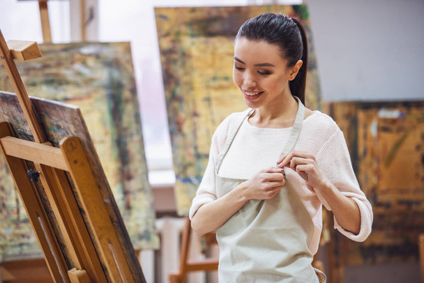 Młoda kobieta piękne malarstwo artysty podczas pracy w studio, uśmiechając się do kamery - Zdjęcie, obraz