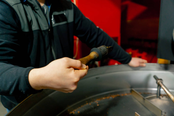 close-up in een kleine roosterfabriek een werknemer staat in de buurt van de roostermachine toezicht op de mate van roosteren - Foto, afbeelding