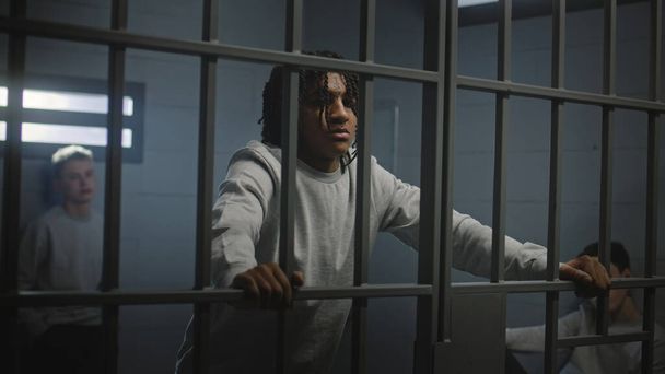 Multi-etnische tieners achter metalen tralies in de cel kijken naar de camera. Jonge gevangenen, criminelen zitten gevangenisstraf uit voor misdaden in de gevangenis. Jeugddetentiecentrum of gevangenis. Portret - Foto, afbeelding