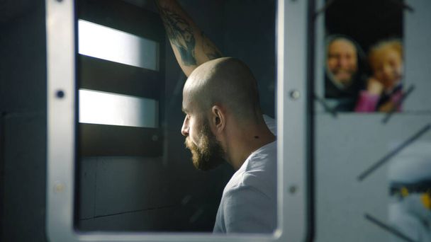 Отражение заключенного-мужчины в зеркале, смотрящего в окно тюремной камеры. Фотографии семьи висят у зеркала. Заключенный отбывает тюремный срок в тюрьме. Исправительный центр или исправительное учреждение. - Фото, изображение