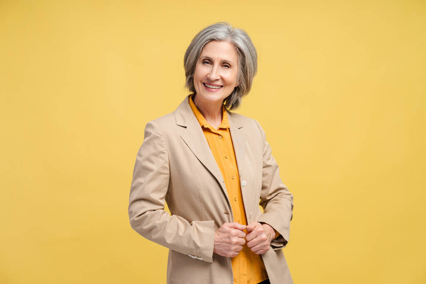 Smiling senior business woman, manager, financier looking at camera isolated on yellow background. Portrait of confident gray haired politician. Successful business, career - Photo, Image