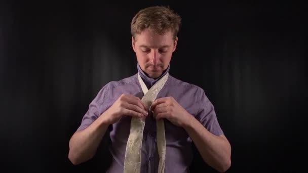 Dapper portret stylowego młodego człowieka dostosowującego ostry biały krawat. Odziany w żywe purpurowe koszulki z luźnym zarostem emanuje chłodnym, ale wyrafinowanym wibracją na minimalnym czarnym tle - Materiał filmowy, wideo