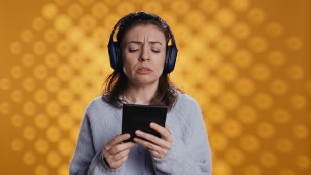 Voice actor frowns while reading ebook, portraying character, studio background. Woman reenacting digital recording of novel, interpreting furious antagonist, reading text from tablet, camera B - Footage, Video