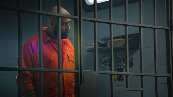 Häftling in orangefarbener Uniform steht hinter Gittern in Gefängniszelle, spricht mit Anwalt und liest Vertrag. Häftling verbüßt Haftstrafe für Verbrechen in Justizvollzugsanstalt Gangster in Haftanstalt. - Foto, Bild