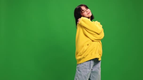 Young beautiful cute woman dressed vibrant casual outfit and hug herself and dancing of joy against vibrant green background. Concept of human emotions, self-expression, style and fashion, self-love. - Footage, Video