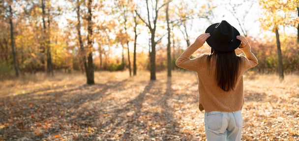 Vista posteriore di una donna bruna con un cappello sullo sfondo di una foresta autunnale. Concetto di svago. Copia spazio - Foto, immagini