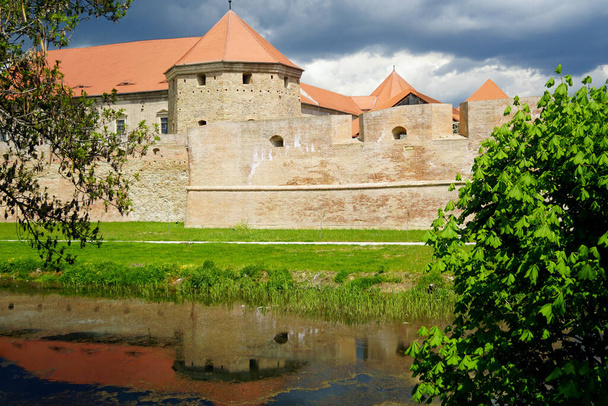 Paisaje de la ciudad de Fagaras en Transilvania, Rumania: un foso con agua y una antigua fortaleza frente a ella con el telón de fondo de un cielo nublado. - Foto, imagen