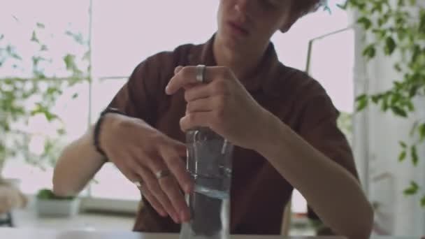 Nuori mies pyyhkäisemällä tinsel pöydältä, juomavesi pullosta ja tunne helmi kun ottaa jatkoksi krapula aamulla kotona - Materiaali, video