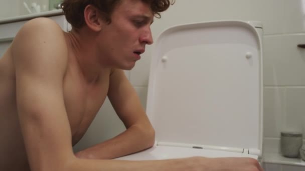 Jeune homme malade se sentant nauséeux appuyé sur les toilettes, puis se reposant dans la salle de bain tout en souffrant de gueule de bois le matin à la maison - Séquence, vidéo