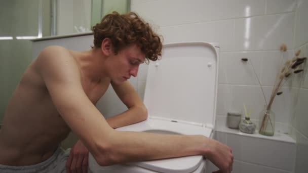Nuori krapula kaveri nojaten wc kylpyhuoneessa tunteessaan pahoinvointia aamulla juhlien jälkeen kotona - Materiaali, video