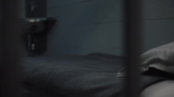 Inmate puts orange prison uniform, bath towel and toilet paper on bed. Guilty criminal or prisoner serves imprisonment term in jail. Detention center or correctional facility. View through metal bars. - Footage, Video