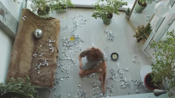 Top down zicht van jonge kater man drinken van water uit fles en liggend op rommelige vloer met verspreid knutsel terwijl het gevoel uitgeput na home party - Video