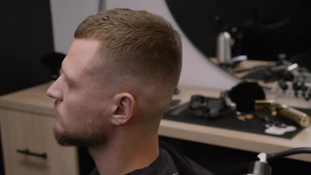 Barber sprays hairstyling product onto man haircut in barbershop closeup. Stylist uses expensive hairspray in grooming salon. Beauty care - Footage, Video