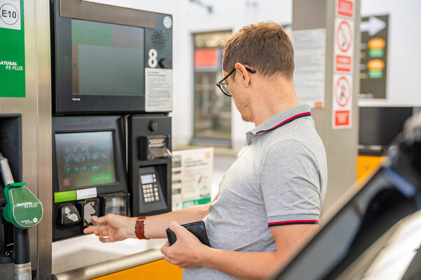 Facet płaci za paliwo kartą kredytową na terminalu samoobsługowej stacji benzynowej w Europie. Wysokiej jakości zdjęcie - Zdjęcie, obraz