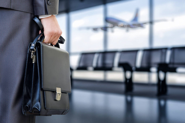 Έννοιες για επαγγελματικά ταξίδια. Επιχειρηματίας κρατώντας ένα χαρτοφύλακα στο φόντο μιας αίθουσας αναμονής αεροδρομίου. - Φωτογραφία, εικόνα