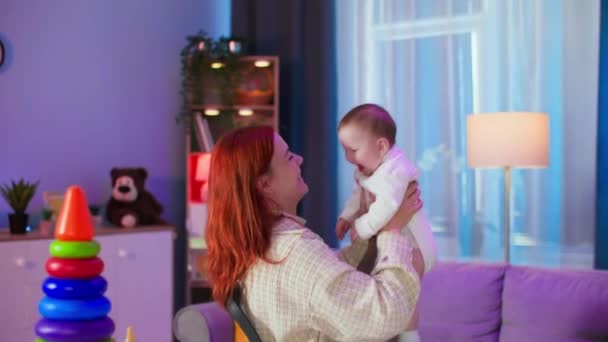 moderna madre joven juega con su hija pequeña, lanza alegremente niño en la parte superior y la atrapa con las manos en una habitación acogedora - Metraje, vídeo